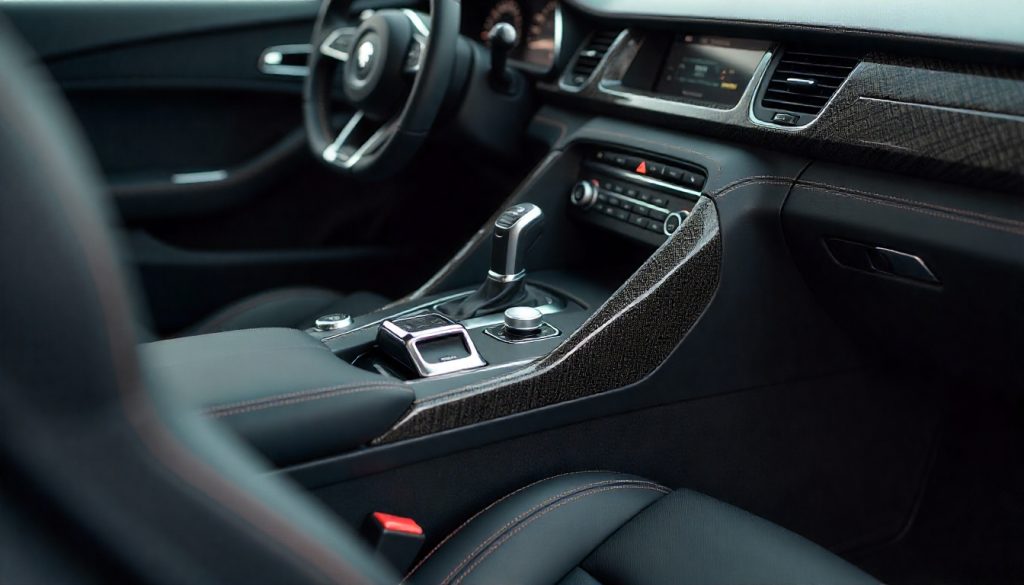 Close-up of handcrafted carbon fiber automotive parts with glossy weave pattern near a luxury sports car interior.