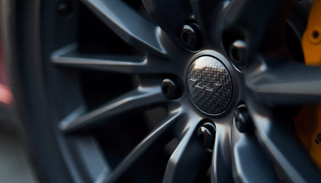 Close-up of a luxury car wheel with carbon fiber valve stem caps paired with matching lug nuts, highlighting premium automotive style and performance.