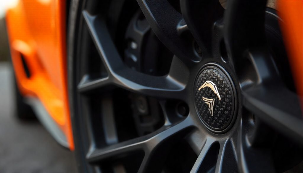 Close-up of carbon fiber tire valve caps on a luxury sports car wheel with dark alloy rim, highlighting premium carbon fiber weave and modern automotive styling.