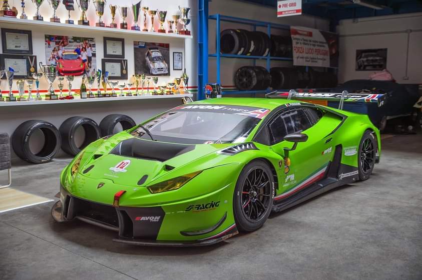 Bright green Lamborghini race car in a garage with tires and tools.