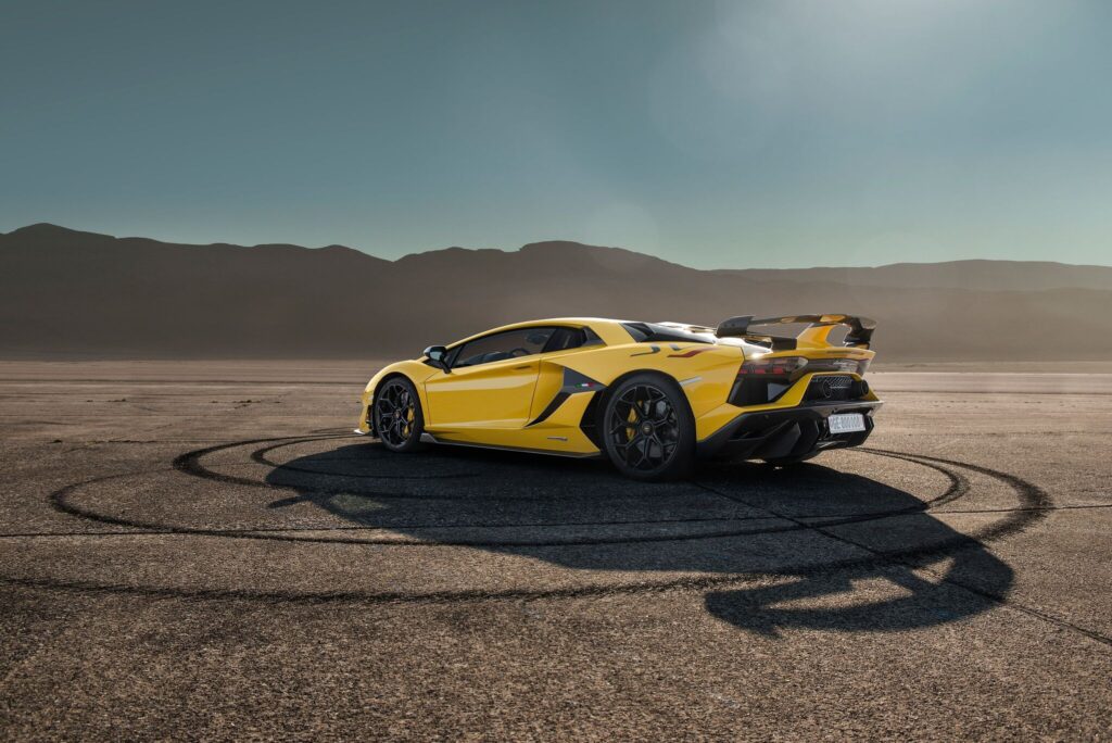Yellow sports car parked on a cracked desert road under a clear sky.